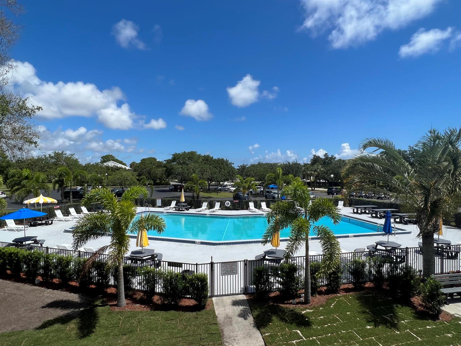 An outdoor swimming pool is surrounded by a fence, palm trees, and lounge chairs — 4310 Gator Trace Circle, Fort Pierce FL 34982, FORT PIERCE, FL