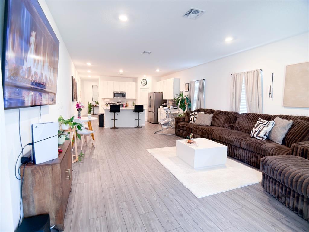 An open-concept living room and kitchen featuring wood-look flooring, a brown sectional, and white cabinetry — 4732 NW 11TH STREET, OCALA, FL