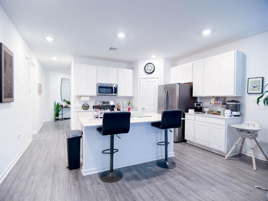 A modern kitchen features white cabinets, stainless steel appliances, a center island, and gray flooring — 4732 NW 11TH STREET, OCALA, FL