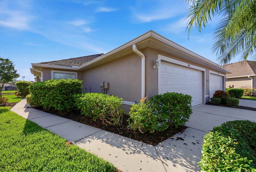 A beige house exterior features a two-car garage, a concrete driveway, and manicured green landscaping — 5968 IBIS COURT, NORTH PORT, FL