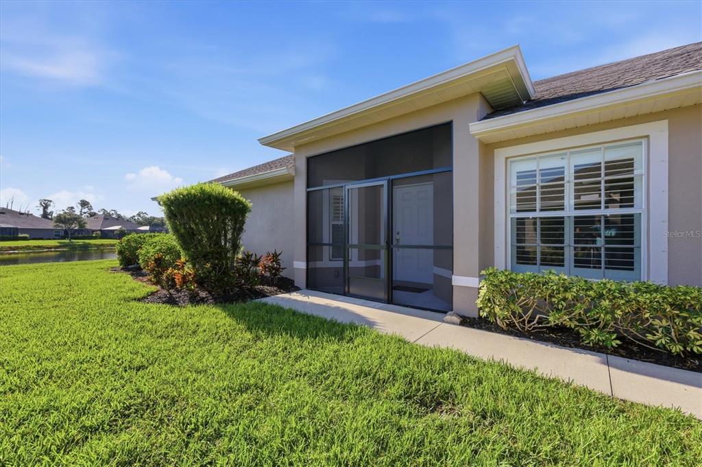 A screened-in entryway leads to a white front door beside a window with shutters — 5968 IBIS COURT, NORTH PORT, FL