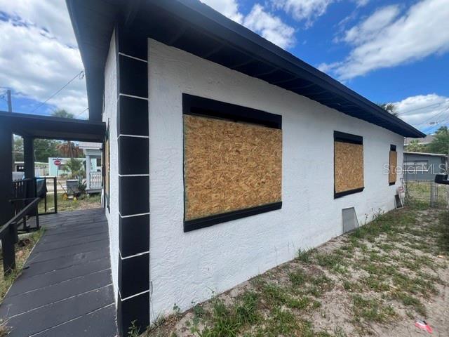 The exterior of a white stucco house features black trim and boarded-up windows — 1106 CARLTON STREET, CLEARWATER, FL