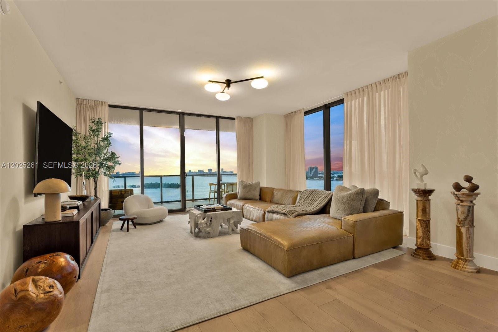 A modern living room features a leather sectional, floor-to-ceiling windows, and a waterfront view — 788 NE 23rd St # 1501, Miami FL 33137, MIAMI, FL