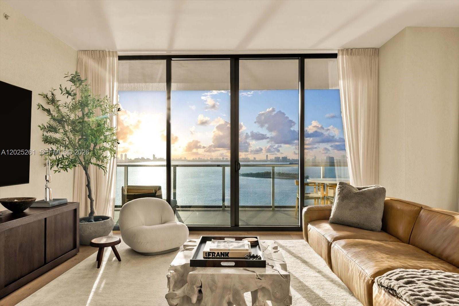 A living room features a leather sofa, a white accent chair, and floor-to-ceiling windows overlooking water — 788 NE 23rd St # 1501, Miami FL 33137, MIAMI, FL
