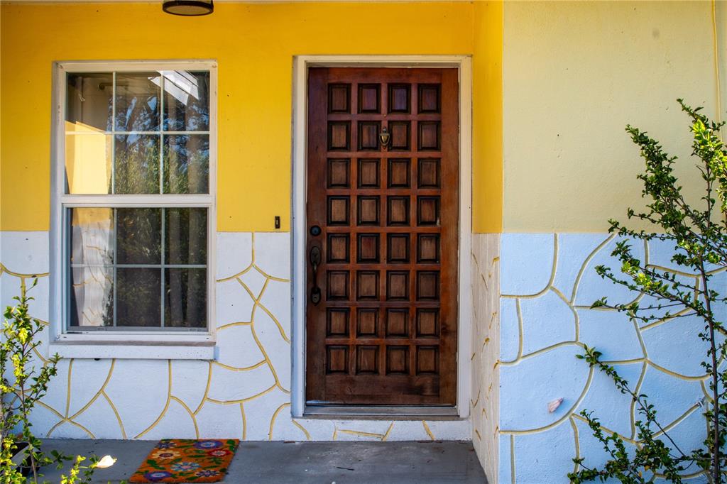 A wooden front door with a grid pattern sits beside a window on a yellow wall — 2766 NAVEL DRIVE, CLEARWATER, FL