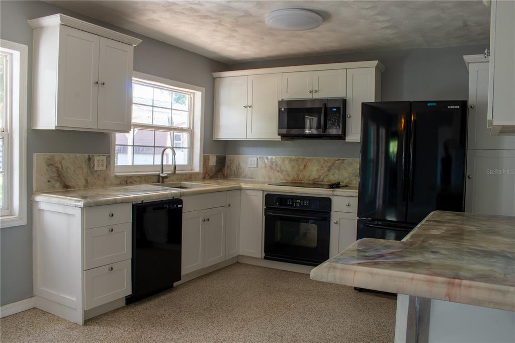 A kitchen with white cabinets, black appliances, and a patterned stone countertop and backsplash — 2766 NAVEL DRIVE, CLEARWATER, FL