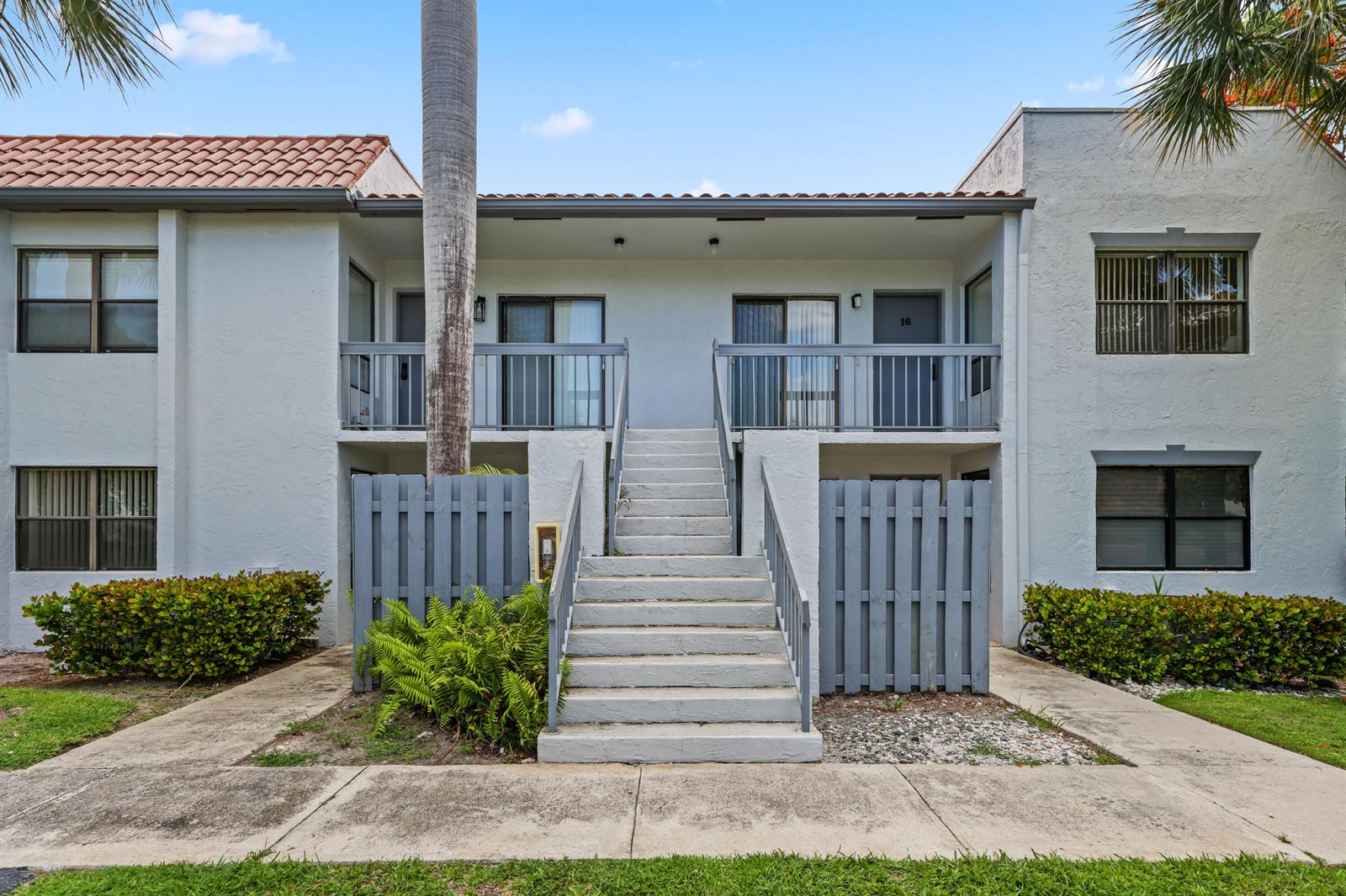 A two-story apartment building exterior features a central concrete staircase leading to upper-level balconies — 3275 Frederick Boulevard # 17u, Delray Beach FL 33483, DELRAY BEACH, FL