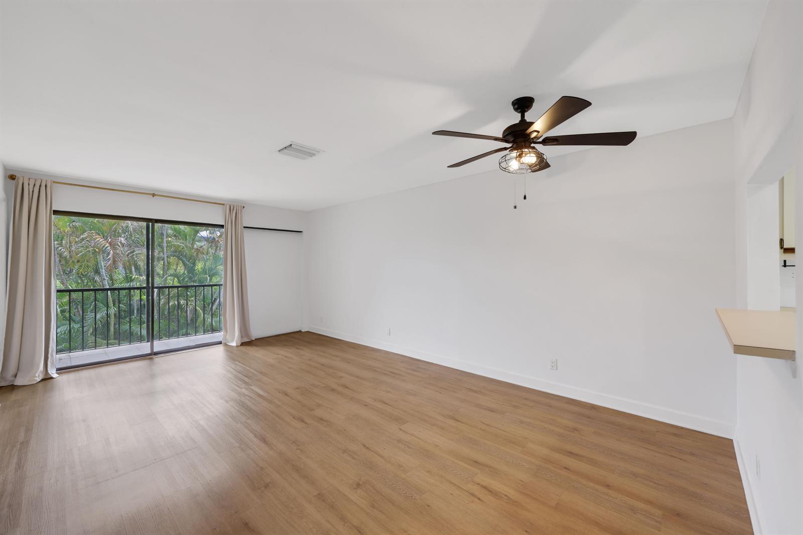 An empty living room features light wood-look flooring, a ceiling fan, and a sliding glass door — 3275 Frederick Boulevard # 17u, Delray Beach FL 33483, DELRAY BEACH, FL