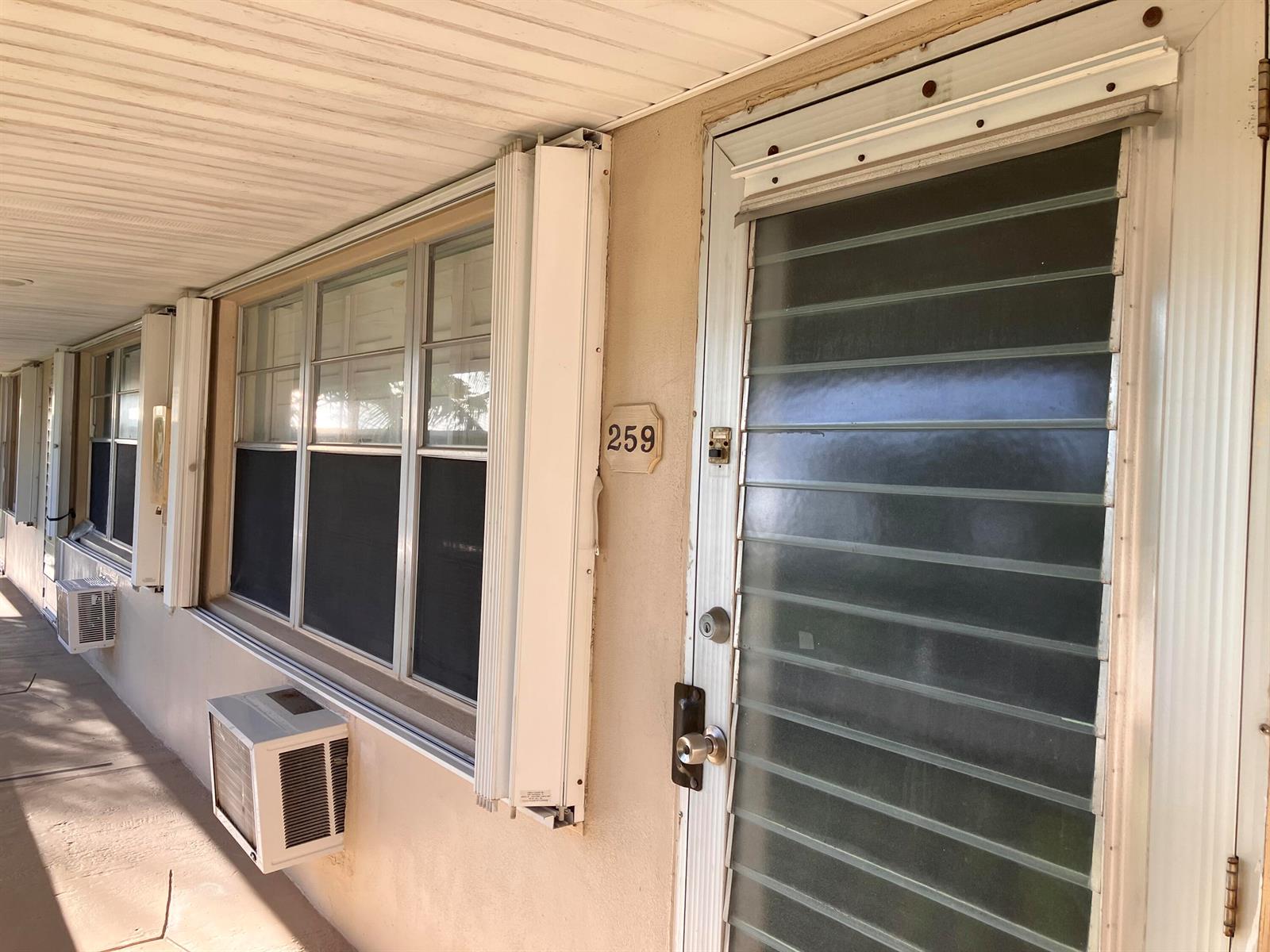Exterior view of a building entrance with a louvered door, windows, and air conditioning units — 259 Sheffield K # 259, West Palm Beach FL 33417, WEST PALM BEACH, FL