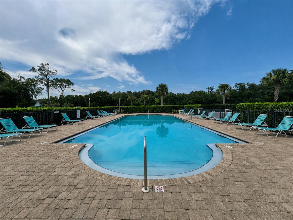 An outdoor swimming pool surrounded by lounge chairs and a paved deck under a blue sky — 2706 SPARTA DRIVE, NEW SMYRNA BEACH, FL