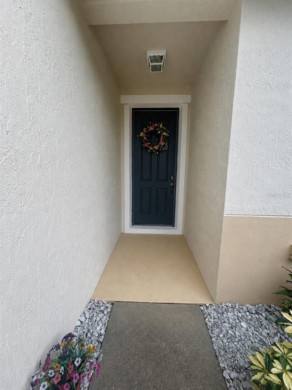 A dark blue front door with a floral wreath sits at the end of a walkway — 2706 SPARTA DRIVE, NEW SMYRNA BEACH, FL