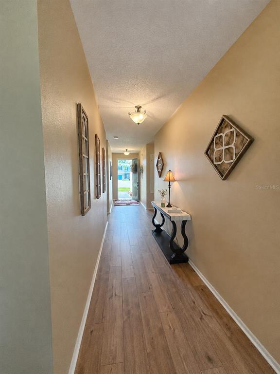 A long hallway features wood-look tile flooring, beige walls, a console table, and wall decor — 2706 SPARTA DRIVE, NEW SMYRNA BEACH, FL