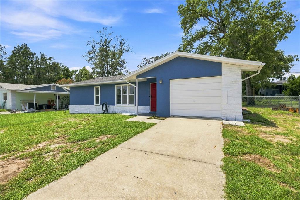 A blue single-story house with a white garage door, red front door, and concrete driveway — 510 S ADAMS STREET, BEVERLY HILLS, FL