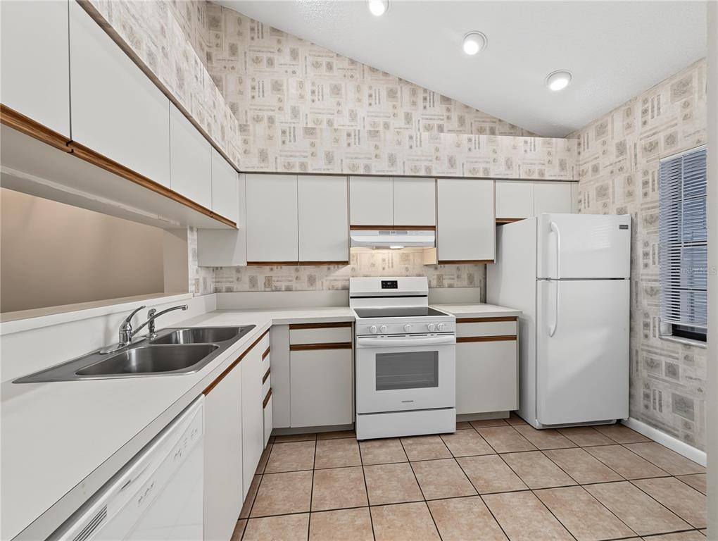 A kitchen with white cabinets, white appliances, patterned wallpaper, and light-colored tile flooring — 4554 MORNINGSIDE UNIT 42, SARASOTA, FL
