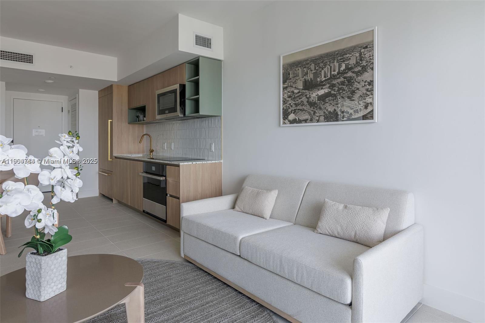 A modern studio apartment features a kitchenette with light wood cabinetry and a beige sofa — 159 NE 6th St # 2404, Miami FL 33132, MIAMI, FL