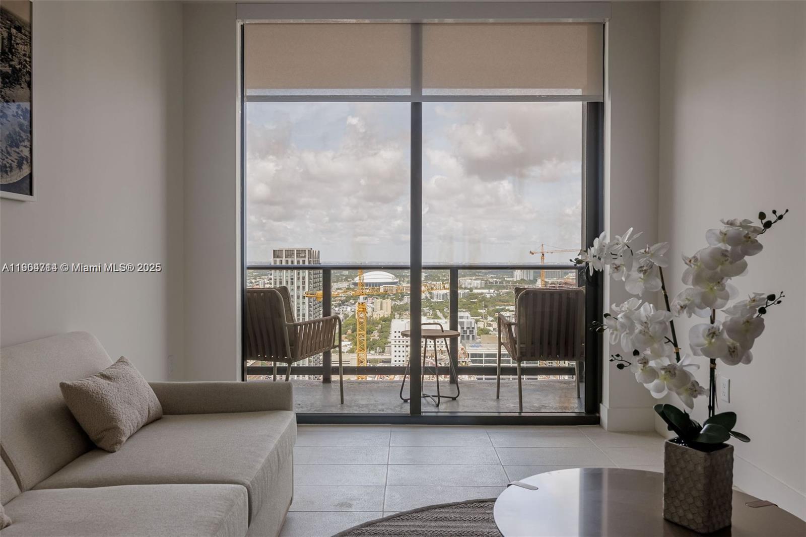 A living room features a beige sofa, a balcony with two chairs, and a city view — 159 NE 6th St # 2404, Miami FL 33132, MIAMI, FL