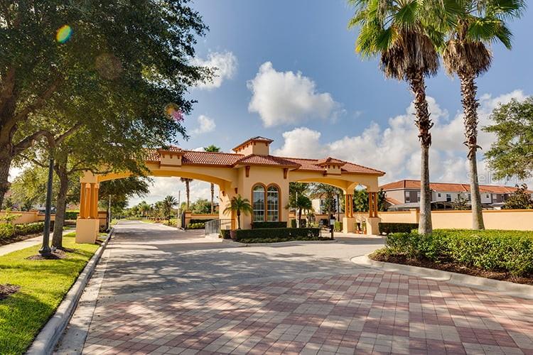 A gated community entrance features a tan stucco structure with a tiled roof and palm trees — 294 MARCELLO BOULEVARD, KISSIMMEE, FL