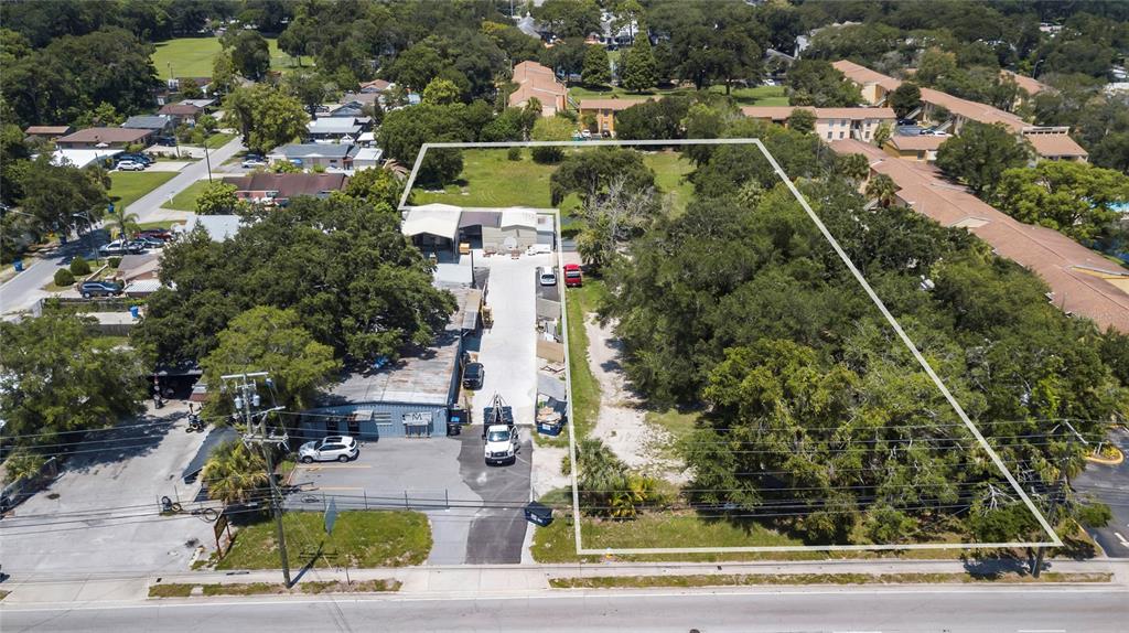 An aerial view shows a commercial property with a warehouse, paved driveway, and adjacent wooded lot — 6010 N ARMENIA AVENUE, TAMPA, FL