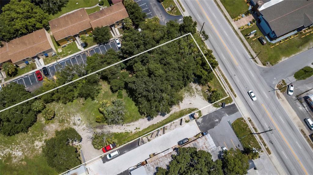 An aerial view shows a vacant, tree-covered lot bordered by a road and parking areas — 6010 N ARMENIA AVENUE, TAMPA, FL