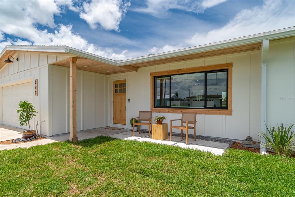 A modern one-story house exterior features white board-and-batten siding, a wood-trimmed window, and a porch — 390 URSA AVENUE, MERRITT ISLAND, FL