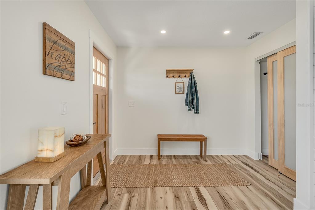 An entryway features a wooden console table, a bench, a coat rack, and wood-look flooring — 390 URSA AVENUE, MERRITT ISLAND, FL