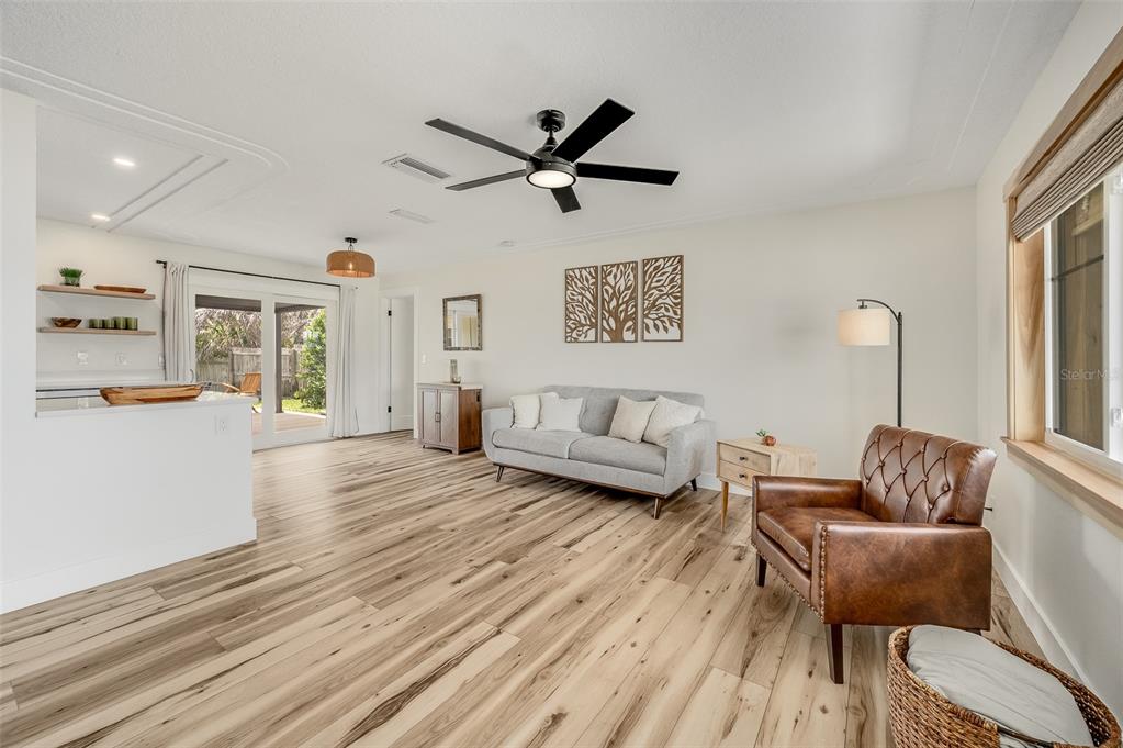 A living room features light wood-look flooring, a gray sofa, and a brown leather armchair — 390 URSA AVENUE, MERRITT ISLAND, FL