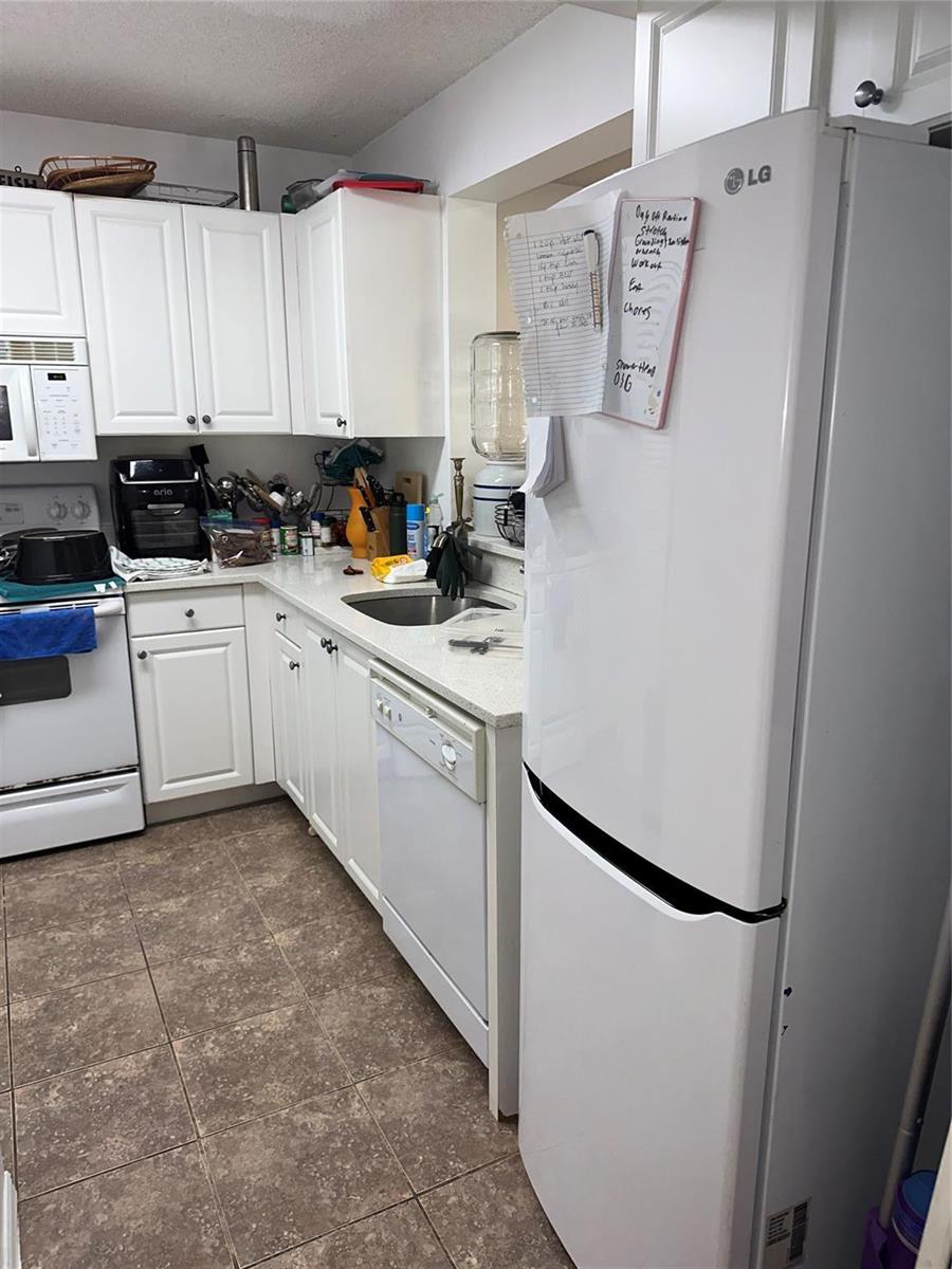 A white kitchen features white cabinets, a dishwasher, a refrigerator, and a tiled floor — 1450 SE 3rd Avenue # 107, Dania Beach FL 33004, DANIA BEACH, FL