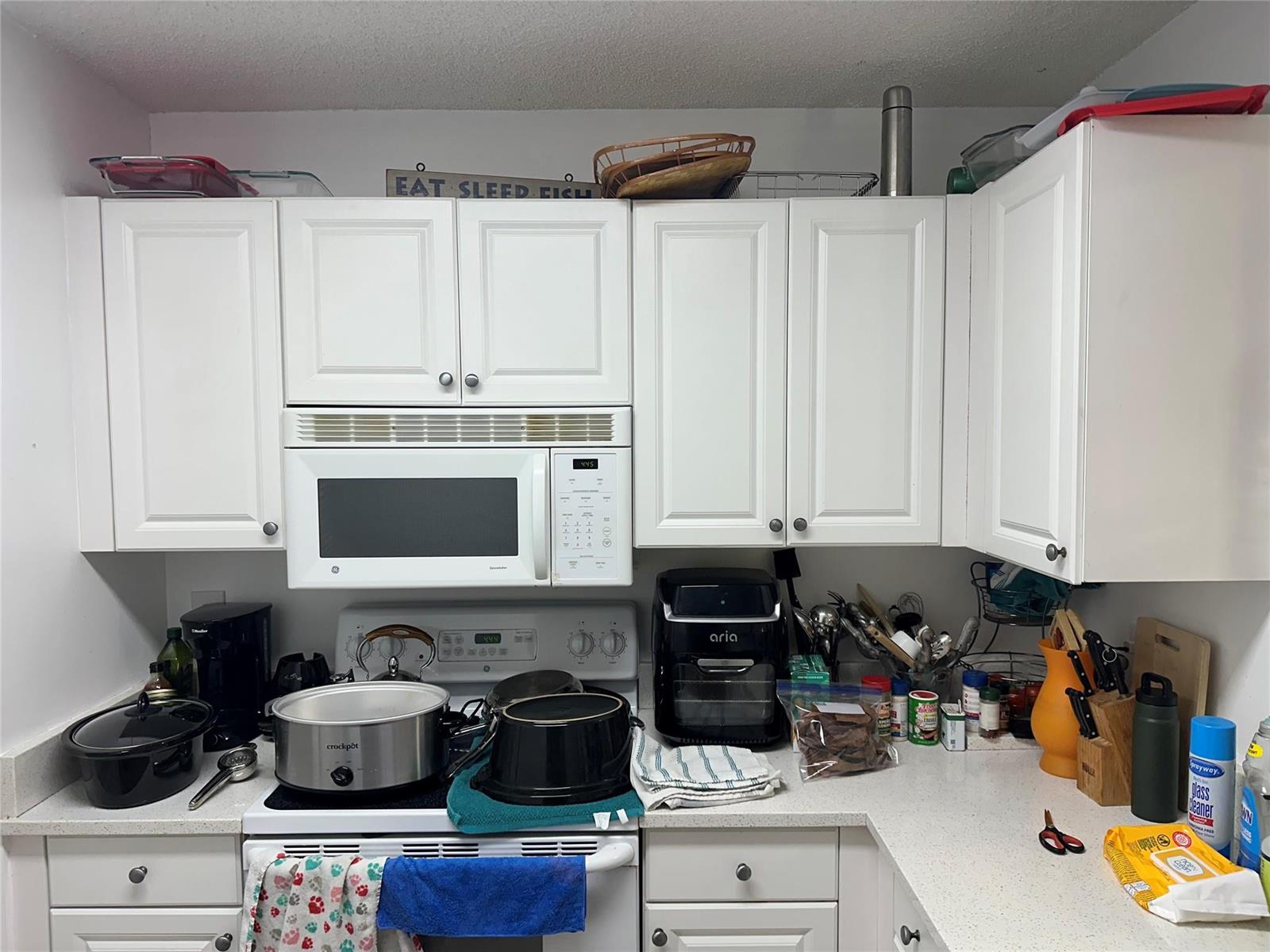 A kitchen features white cabinets, a microwave over a stove, and various countertop appliances — 1450 SE 3rd Avenue # 107, Dania Beach FL 33004, DANIA BEACH, FL