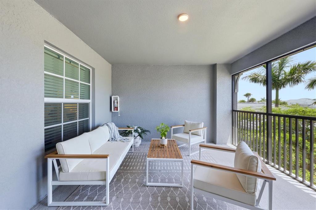 A covered balcony features white patio furniture, a wooden coffee table, and a patterned rug — 12580 GALAPAGOS COURT UNIT #204, VENICE, FL