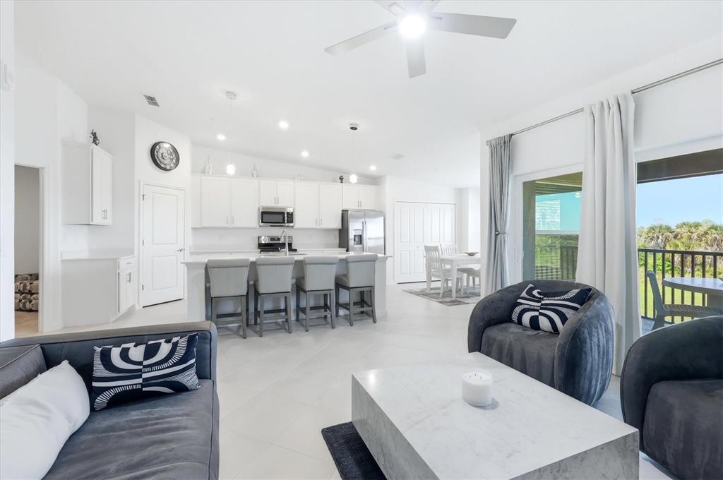 A modern open-concept living room and kitchen featuring white cabinetry, tile floors, and gray furniture — 12580 GALAPAGOS COURT UNIT #204, VENICE, FL