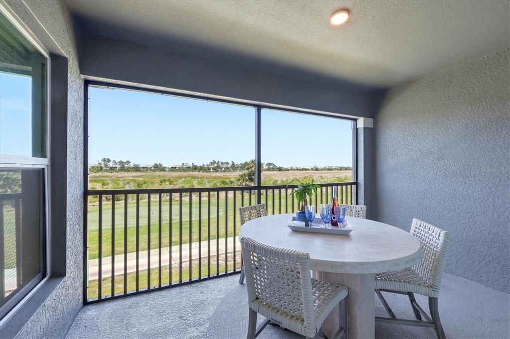 A covered balcony features a round table with chairs overlooking a golf course and field — 12580 GALAPAGOS COURT UNIT #204, VENICE, FL