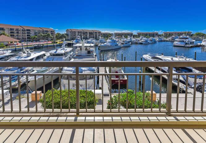 A balcony overlooks a marina filled with yachts and large residential buildings under a clear sky — 2601 Marina Isle Way # 303, Jupiter FL 33477, JUPITER, FL