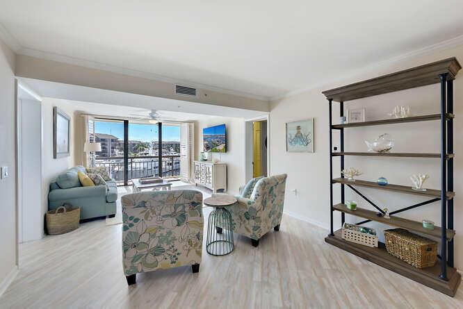 A living room with light wood floors, two patterned armchairs, a blue sofa, and shelving — 2601 Marina Isle Way # 303, Jupiter FL 33477, JUPITER, FL