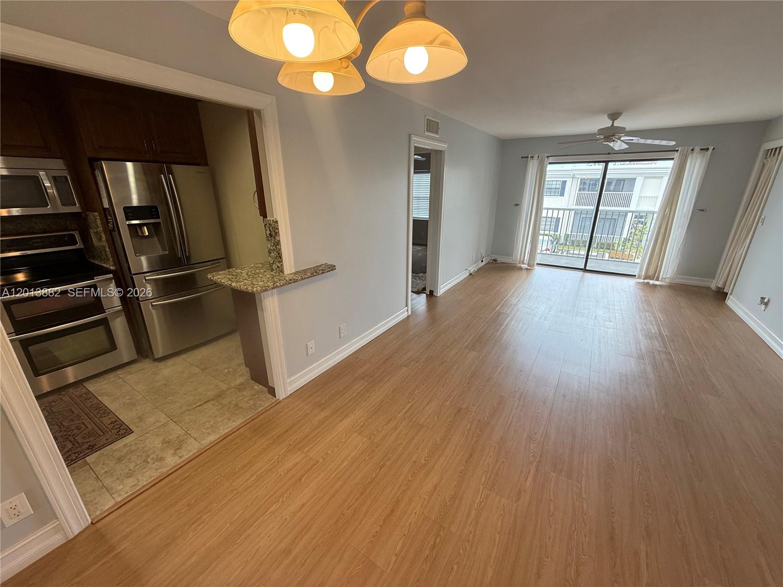 A kitchen with stainless steel appliances opens into a living area with wood-look flooring — 170 Cypress Club Dr # 733, Pompano Beach FL 33060, POMPANO BEACH, FL