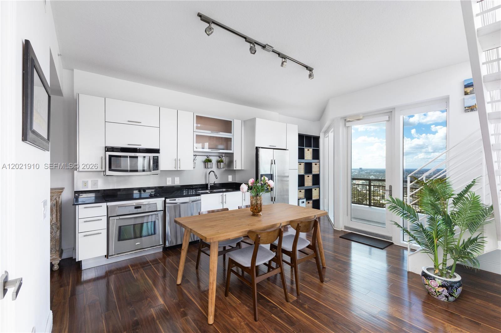 A modern kitchen features white cabinetry, stainless steel appliances, a wooden dining table, and balcony access — 60 SW 13th St # 4613, Miami FL 33130, MIAMI, FL