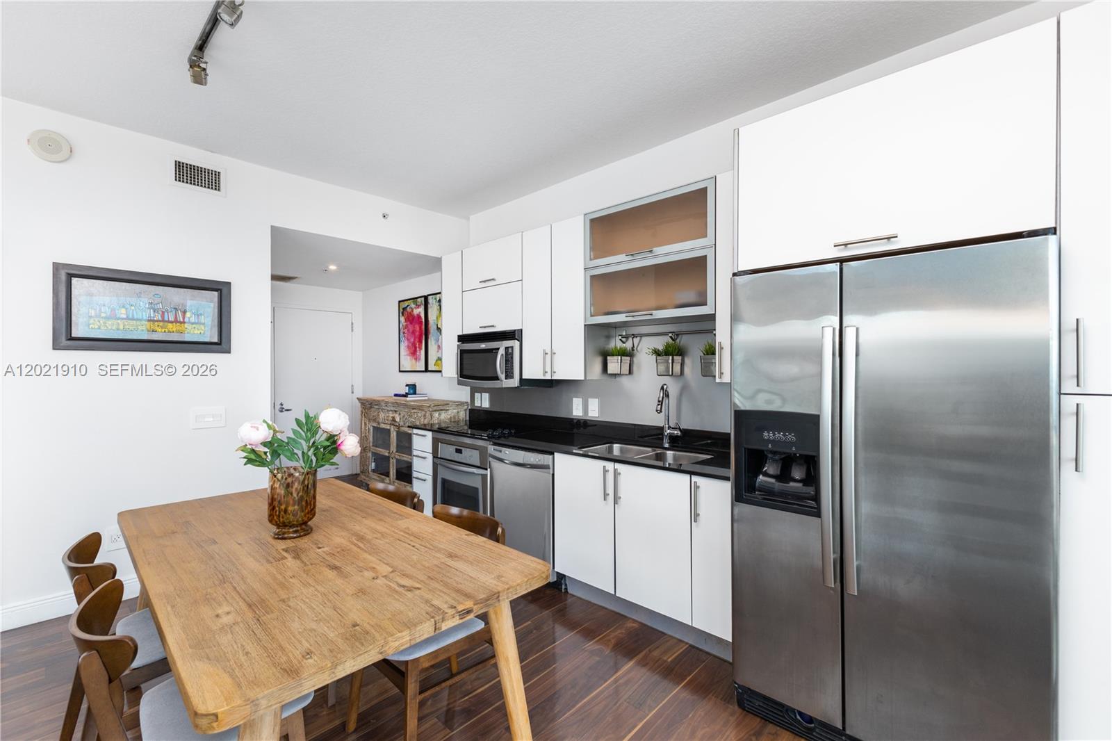 A kitchen features white cabinetry, stainless steel appliances, a black countertop, and a wooden table — 60 SW 13th St # 4613, Miami FL 33130, MIAMI, FL