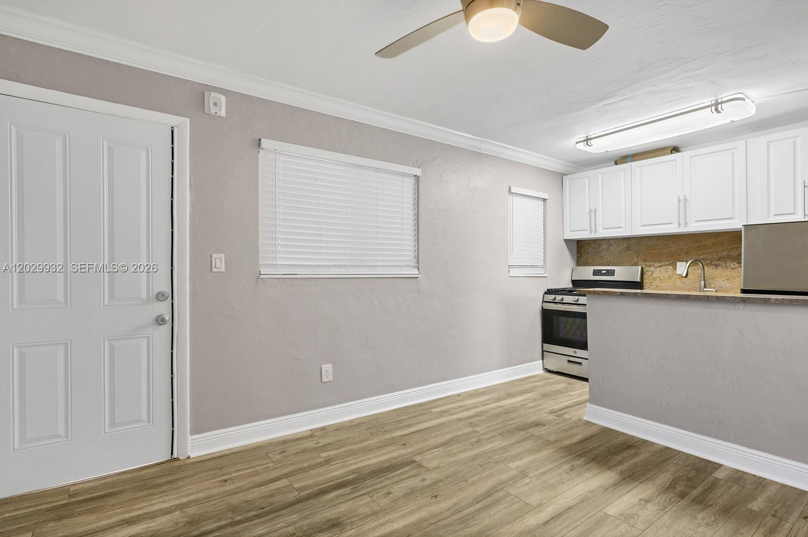 A kitchen with white cabinets and stainless steel appliances opens into a living area — 1014 Salzedo St # 211, Coral Gables FL 33134, CORAL GABLES, FL