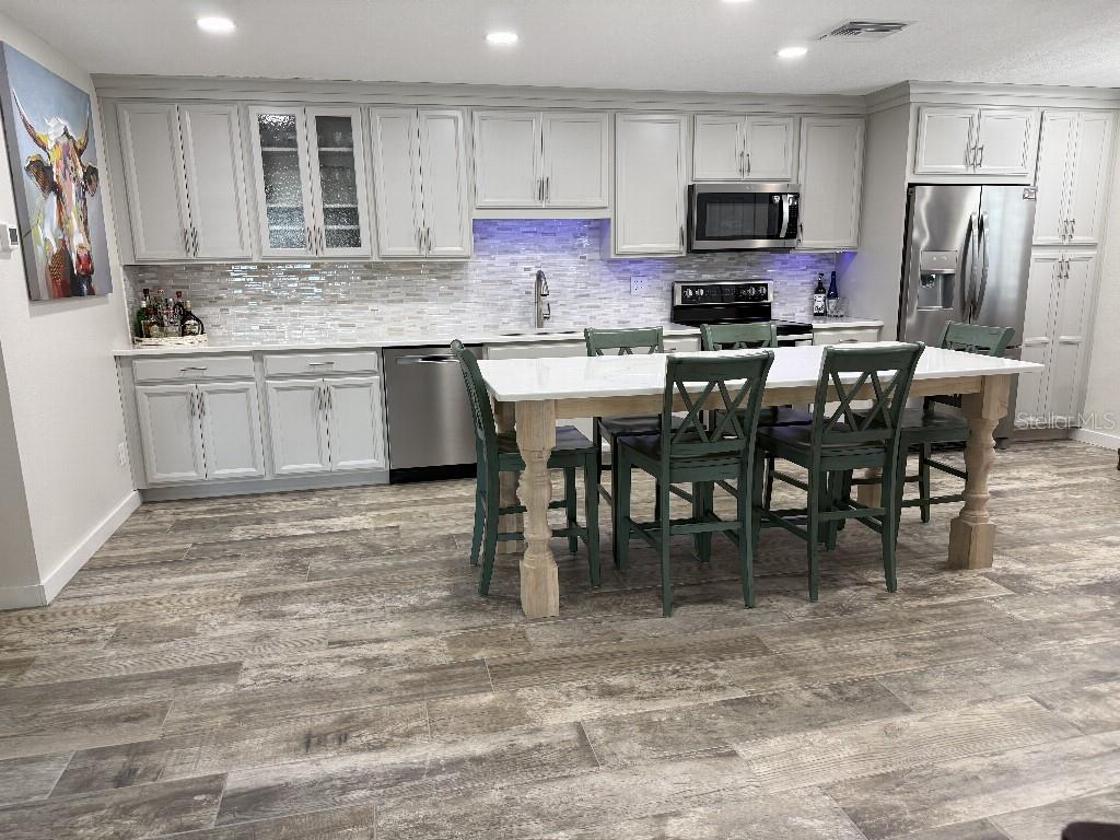 A kitchen features light gray cabinetry, a white island with green chairs, and wood-look flooring — 3323 TEESIDE DRIVE, NEW PORT RICHEY, FL