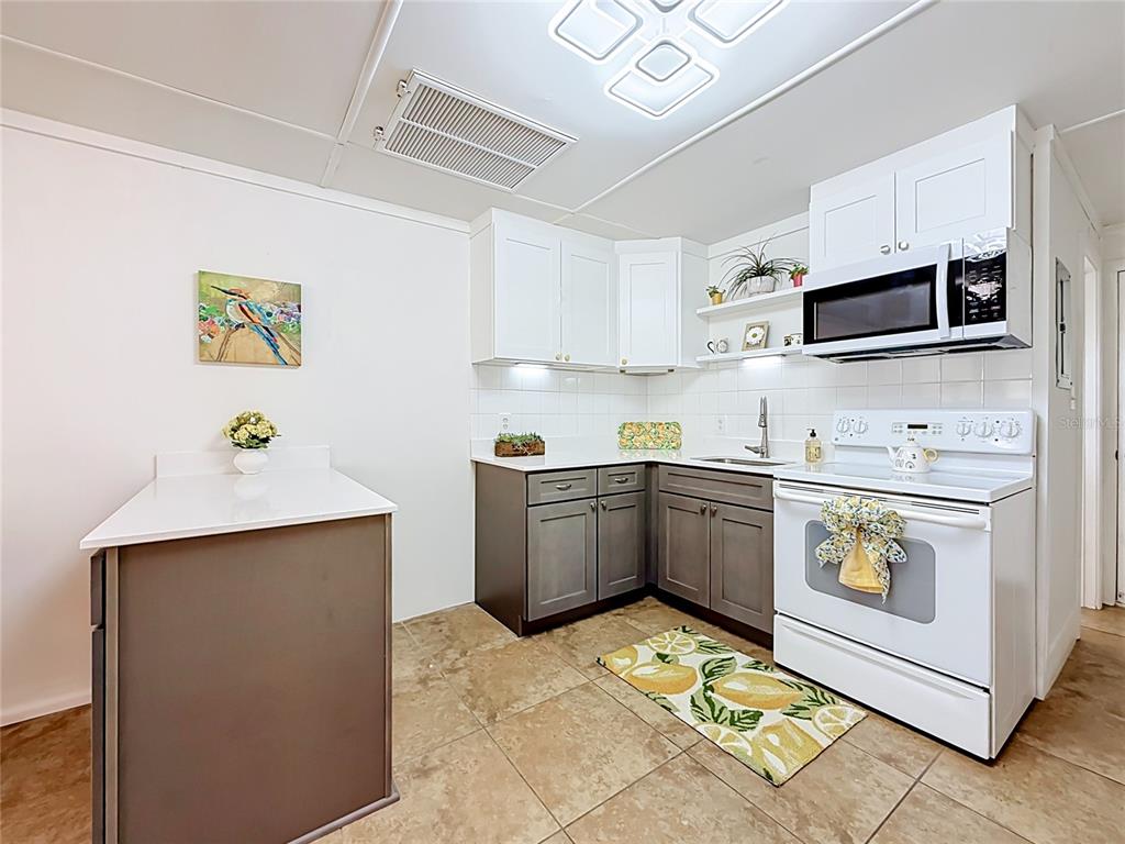 A kitchen features white upper cabinets, gray lower cabinets, white countertops, and tile flooring — 10301 US HIGHWAY 27 UNIT 22, CLERMONT, FL