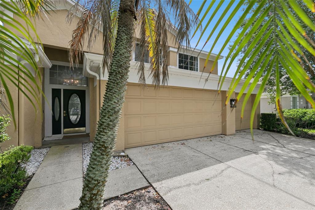 A two-story house exterior features a tan stucco facade, a multi-car garage, and a palm tree — 7800 SAINT GILES PLACE, ORLANDO, FL