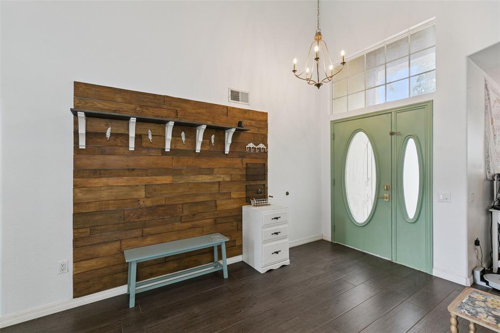 An entryway features a wood-paneled accent wall, a bench, a small cabinet, and green doors — 7800 SAINT GILES PLACE, ORLANDO, FL