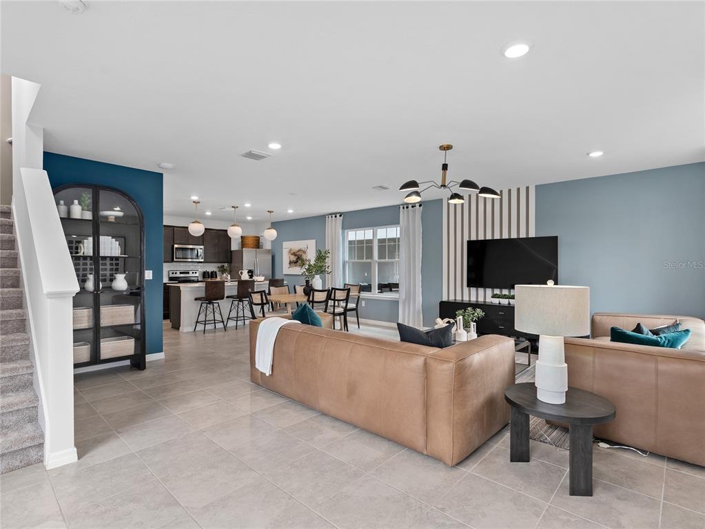 An open-concept living room and kitchen feature blue walls, a leather sofa, and tile flooring — 16827 EVERMORE ALLEY, WINTER GARDEN, FL