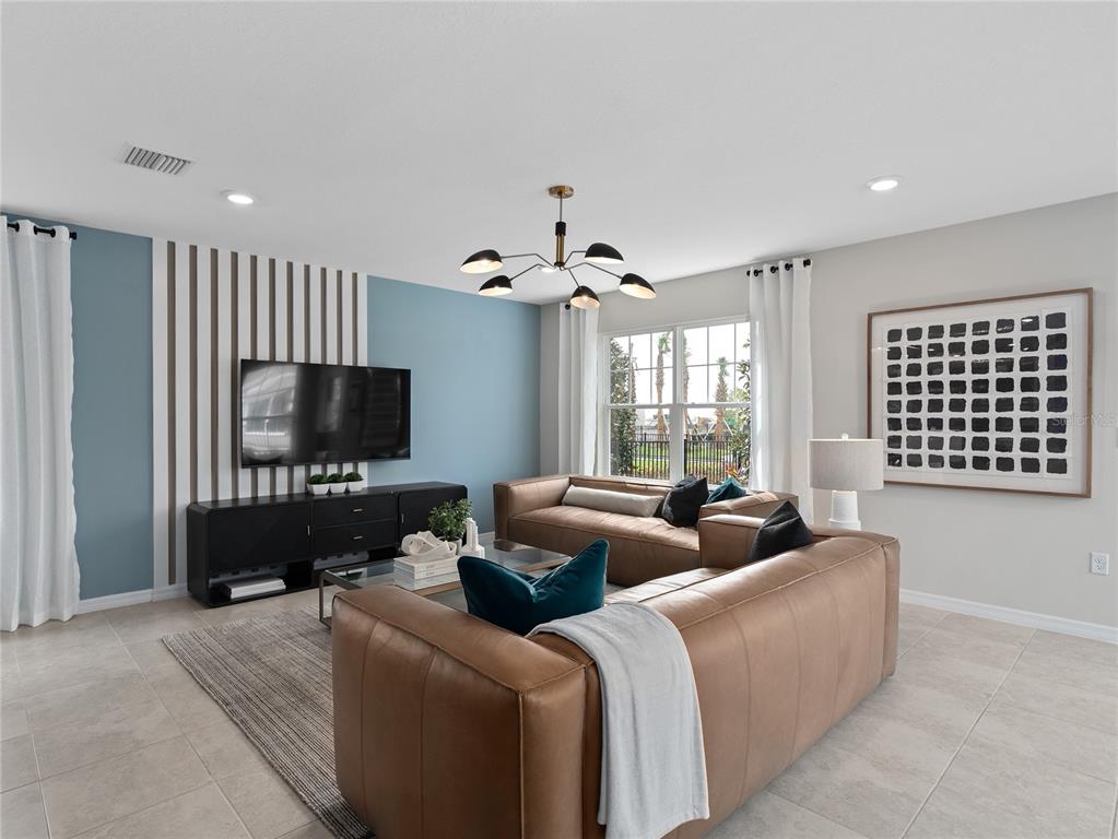 A living room features two leather sofas, a blue accent wall with vertical slats, and tile flooring — 16827 EVERMORE ALLEY, WINTER GARDEN, FL