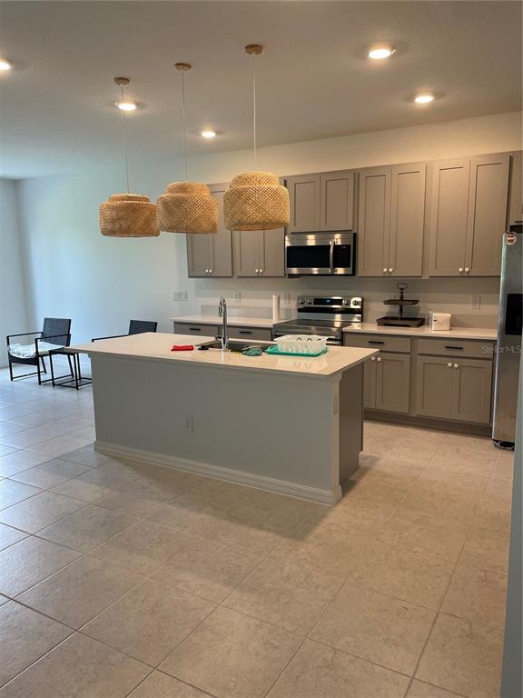A kitchen features a central island, gray cabinetry, stainless steel appliances, and three woven pendant lights — 1731 SANIBEL DR, DAVENPORT, FL