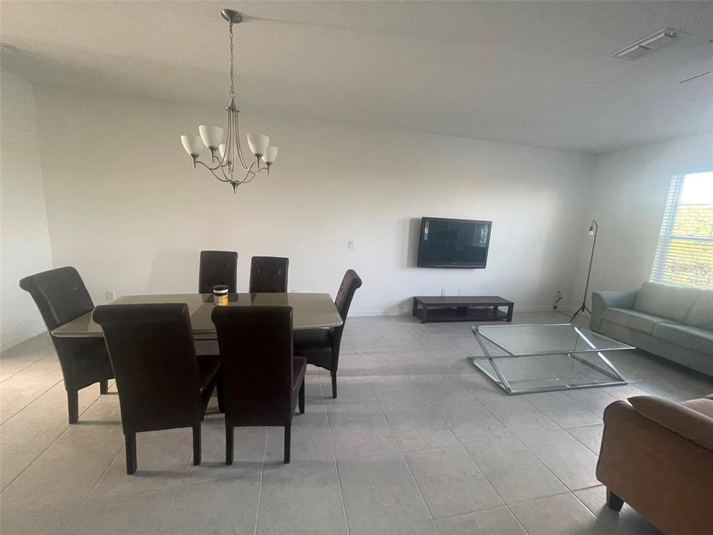 A dining area and living room with tile flooring, a chandelier, and a wall-mounted television — 1731 SANIBEL DR, DAVENPORT, FL