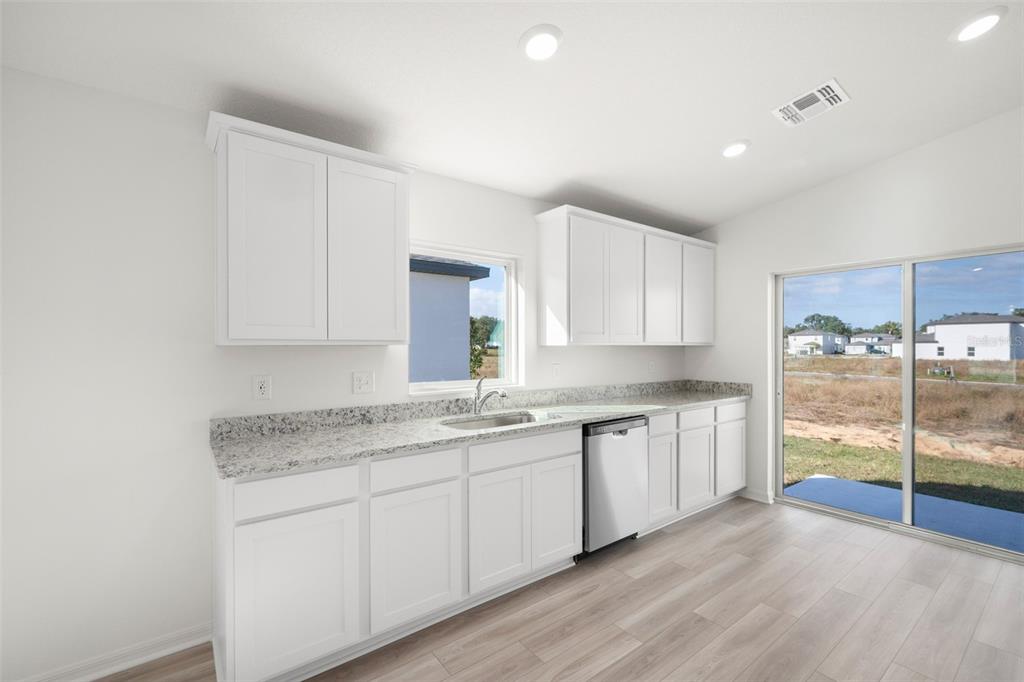 A kitchen with white cabinets, granite countertops, stainless steel dishwasher, and sliding glass patio doors — 13331 TULA LOOP, ASTATULA, FL