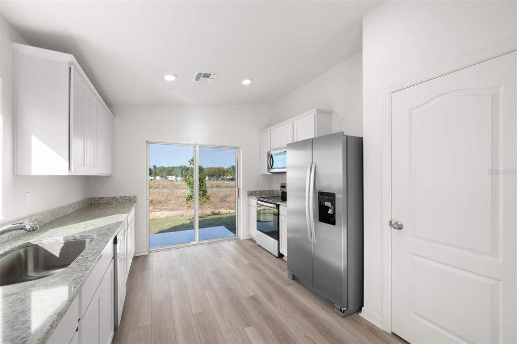 A kitchen with white cabinets, granite countertops, stainless steel appliances, and a sliding glass door — 13331 TULA LOOP, ASTATULA, FL
