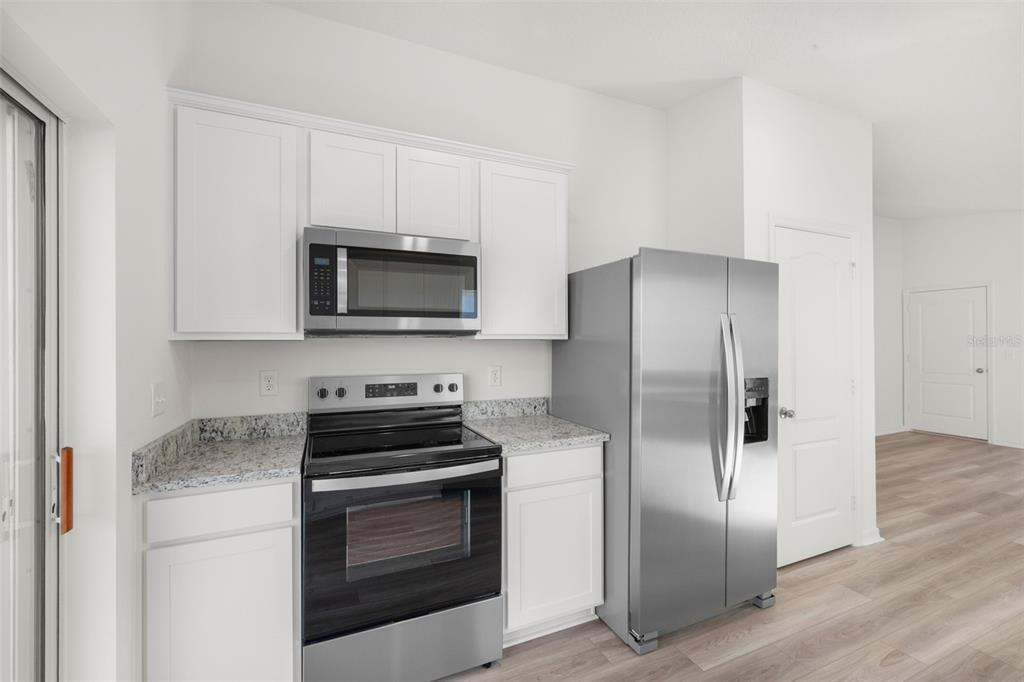 A kitchen features white cabinets, granite countertops, stainless steel appliances, and light wood-look flooring — 13331 TULA LOOP, ASTATULA, FL
