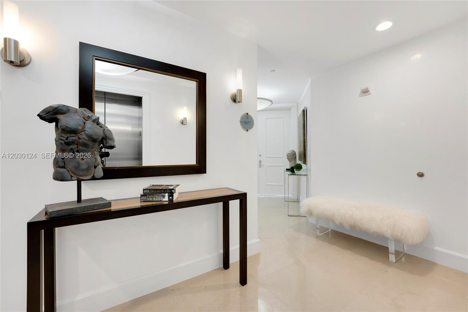 A modern entryway features a console table, a mirror, a sculpture, and a fur bench — 5959 Collins Ave # 807, Miami Beach FL 33140, MIAMI BEACH, FL