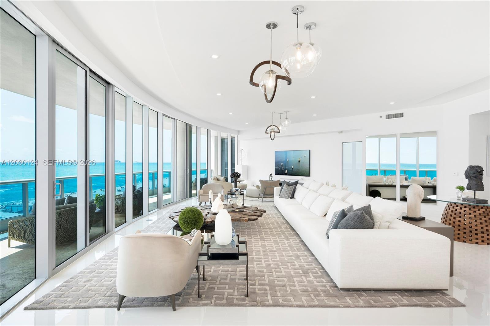 A bright, modern living room features a large white sofa, wood coffee table, and floor-to-ceiling windows — 5959 Collins Ave # 807, Miami Beach FL 33140, MIAMI BEACH, FL